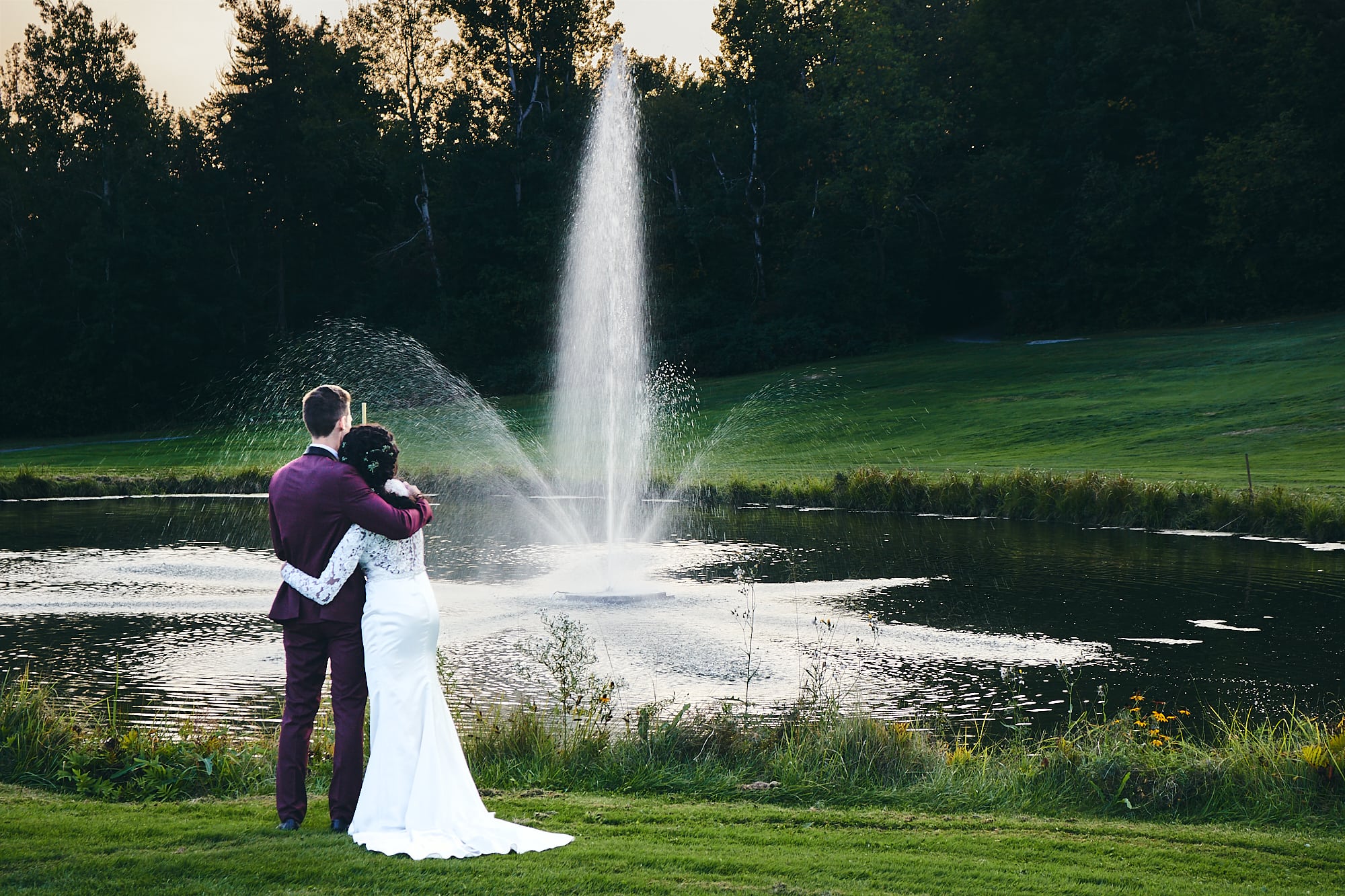 Couple de mariés près de l'étang avec fontaine en arrière-plan.