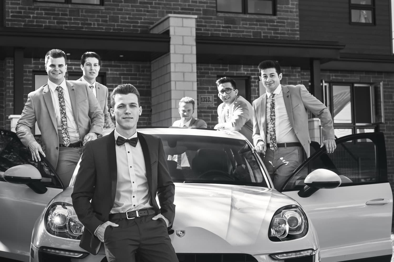 Groupe d'hommes en costume devant une voiture de luxe lors d'un mariage.