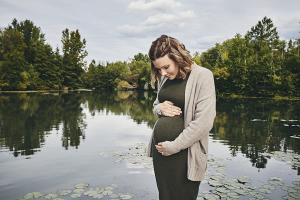 Femme enceinte près d'un lac avec nature environnante.